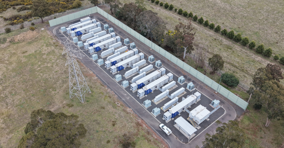 Aerial view of a battery energy storage system (BESS) facility situated next to transmission towers and power lines, highlighting BESS site selection and safety setback compliance.