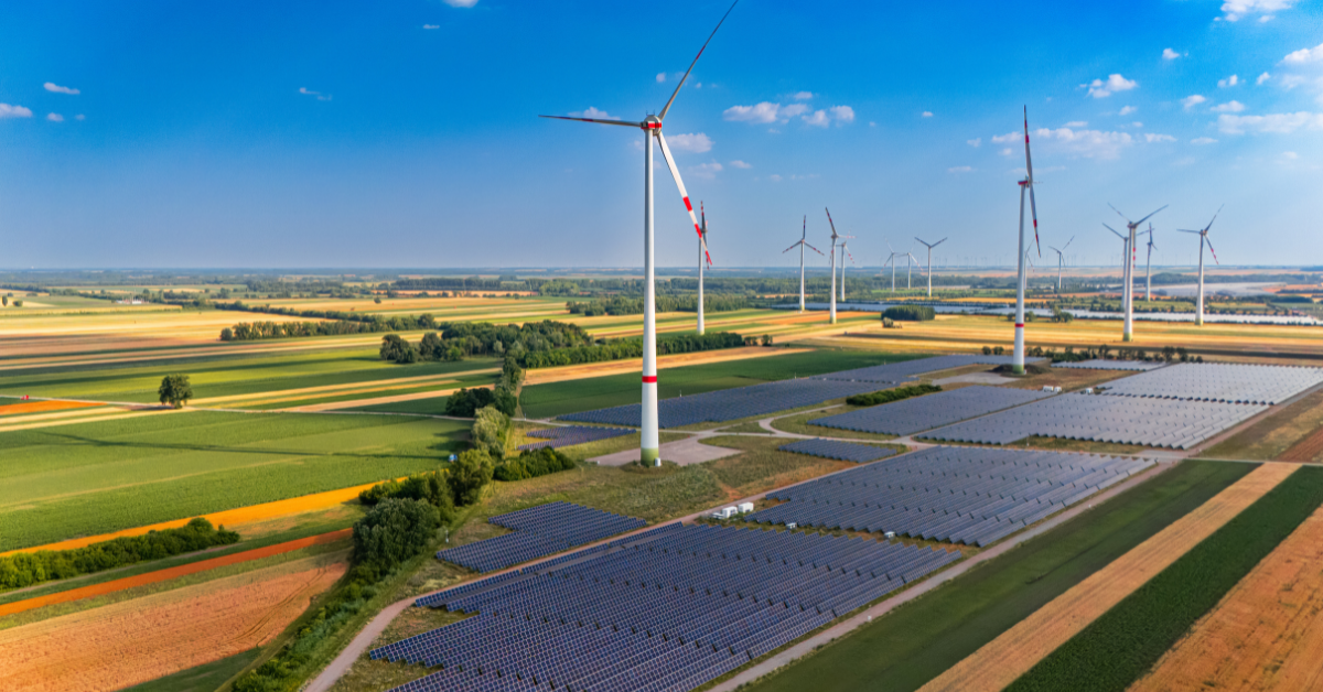 Aerial landscape of a utility-scale solar farm and wind turbines co-existing on agricultural crop fields, highlighting renewable energy land requirements and community acceptance.